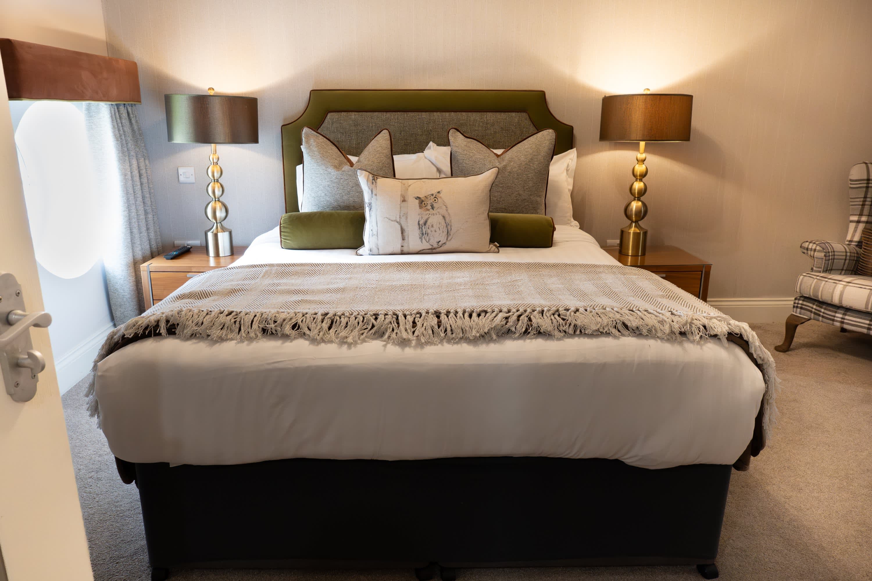 Merrydale Manor bedroom with deep green upholstered headboard, gold globe table lamps and warm amber accent lighting