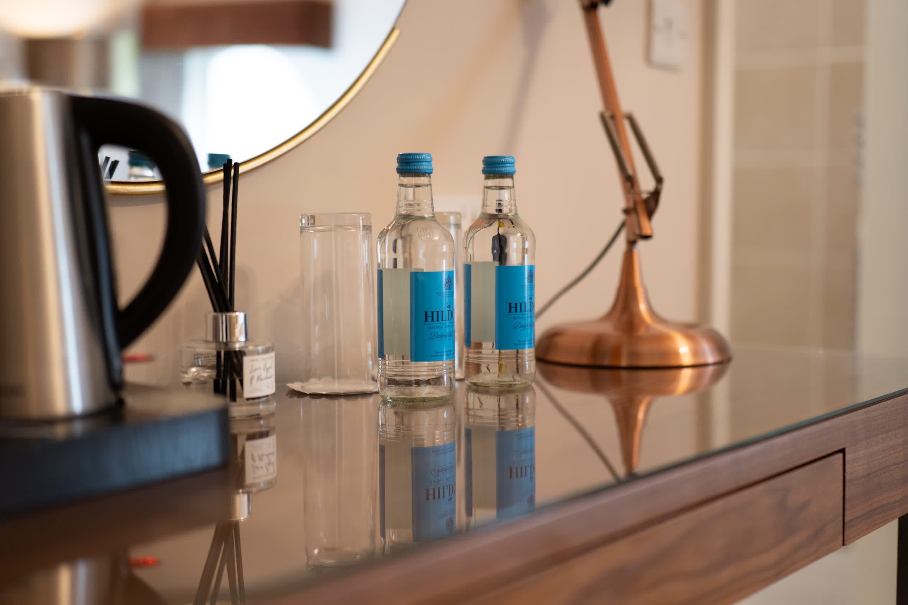 Merrydale Manor in-room hospitality detail with artisan water bottles, glassware, reed diffuser and copper accent lamp