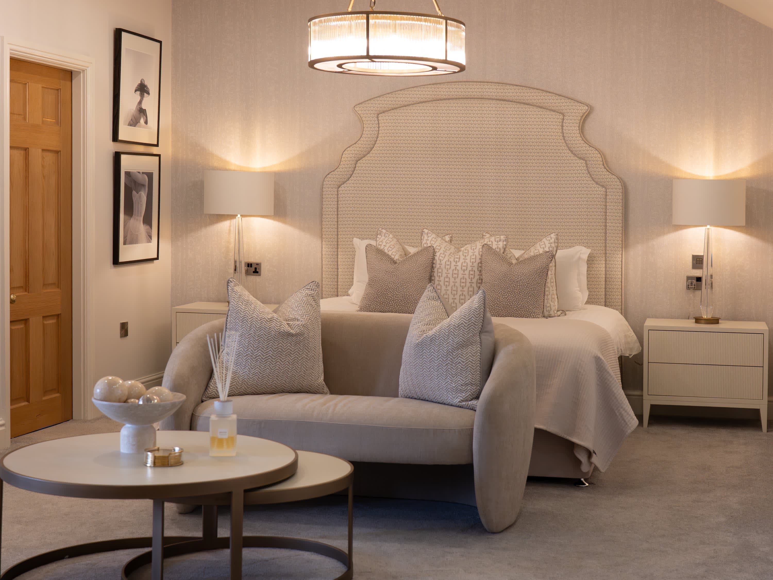 Merrydale Manor luxury suite featuring ornate cream headboard, round pendant chandelier, curved sofa and styled coffee table