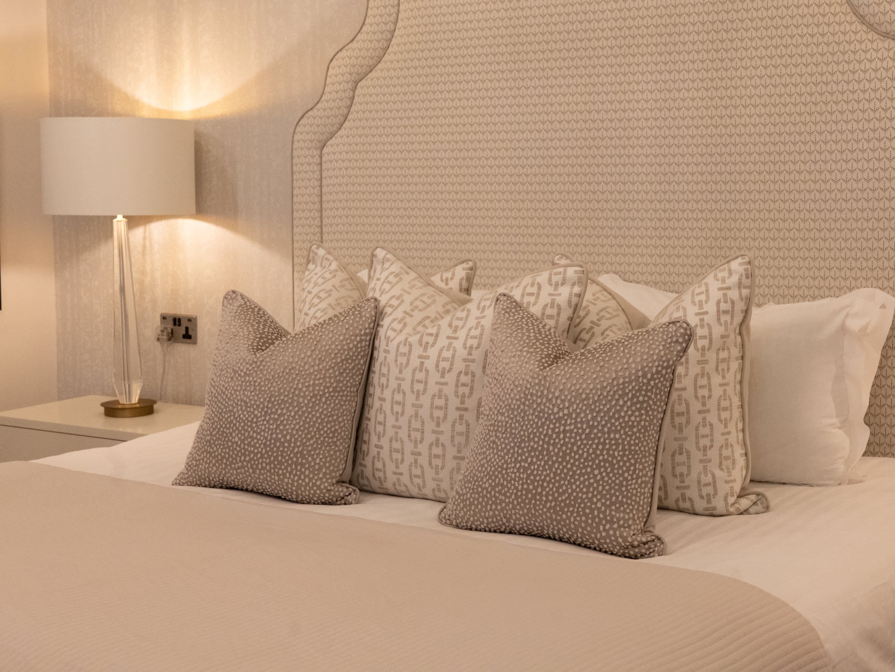 Close-up of Merrydale Manor bed with ornate cream upholstered headboard and layered decorative cushions