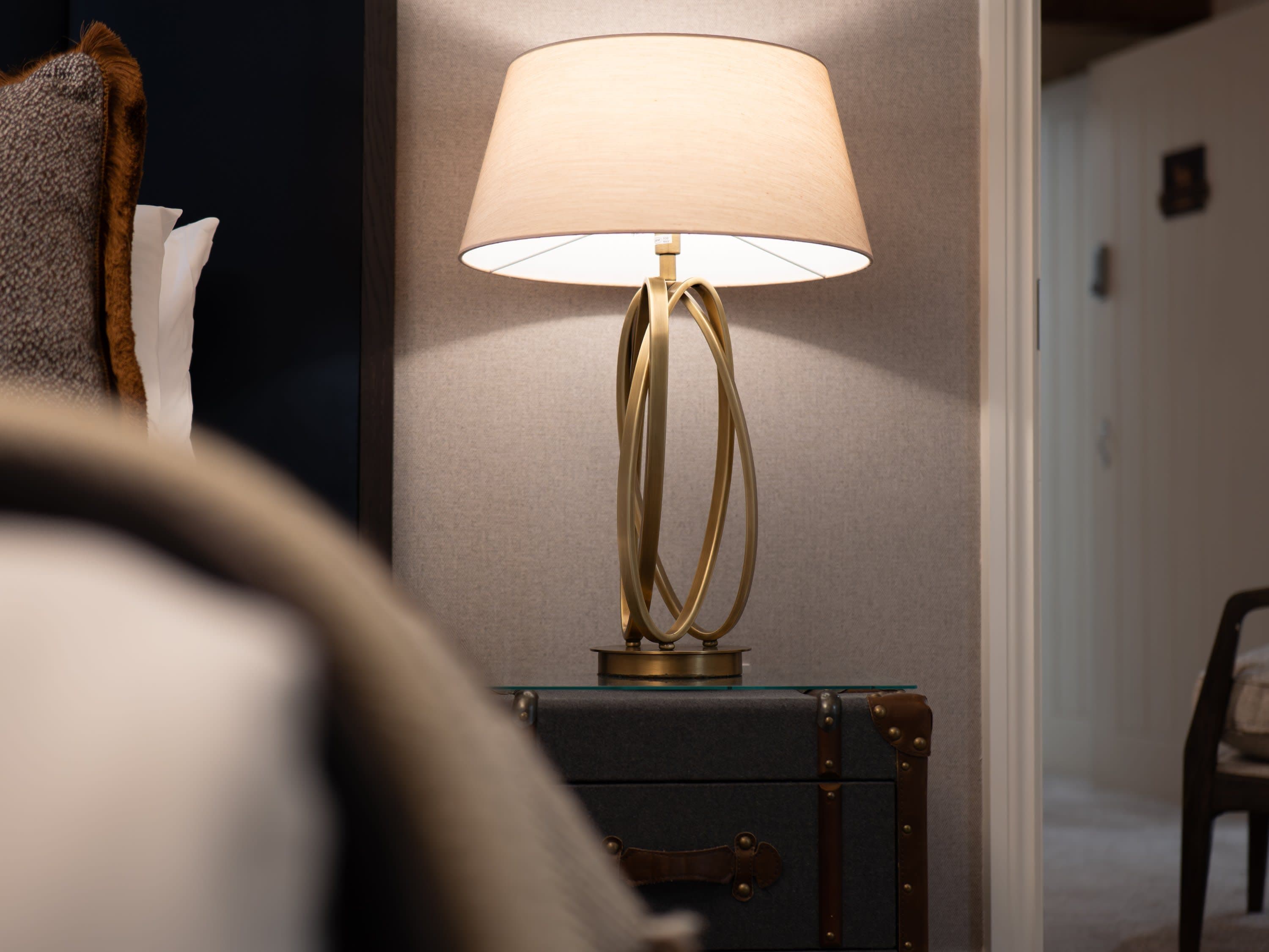 Merrydale Manor bedroom bedside detail with brass ring table lamp positioned on a vintage leather trunk nightstand