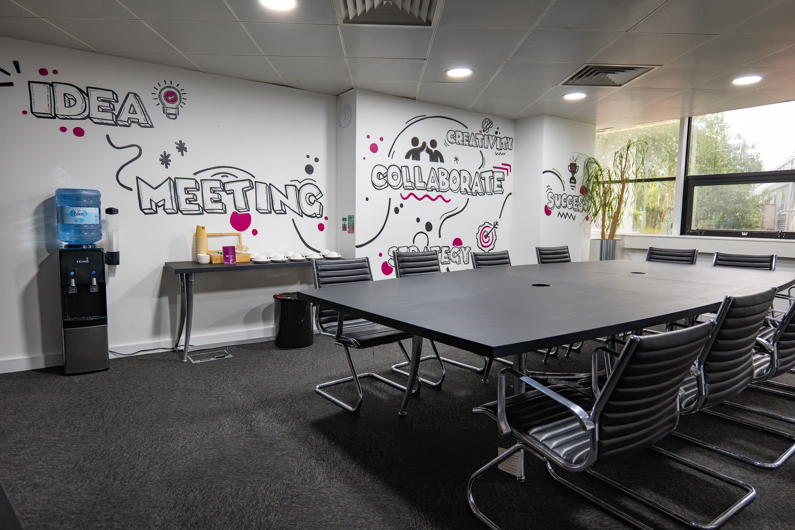 Wide view of the Genesis Centre boardroom with collaboration mural and full conference table layout, Birchwood Warrington