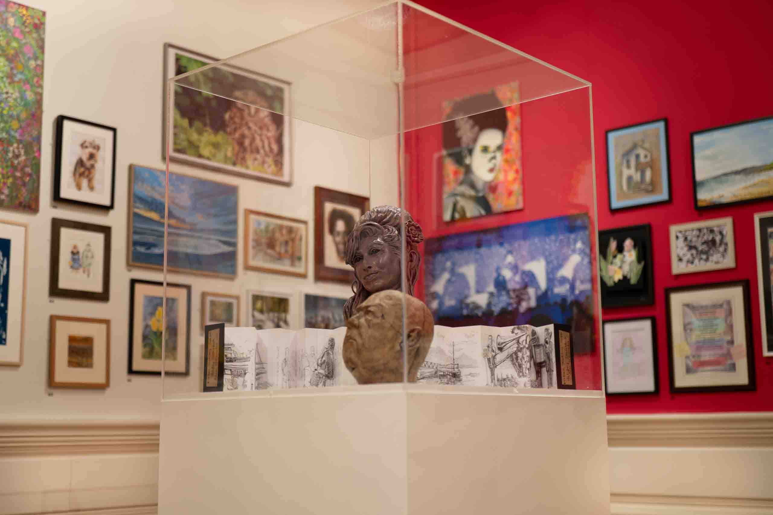 Harris Museum Open Exhibition 2026 — glass display case containing bronze and terracotta bust sculpture with red wall artworks visible behind