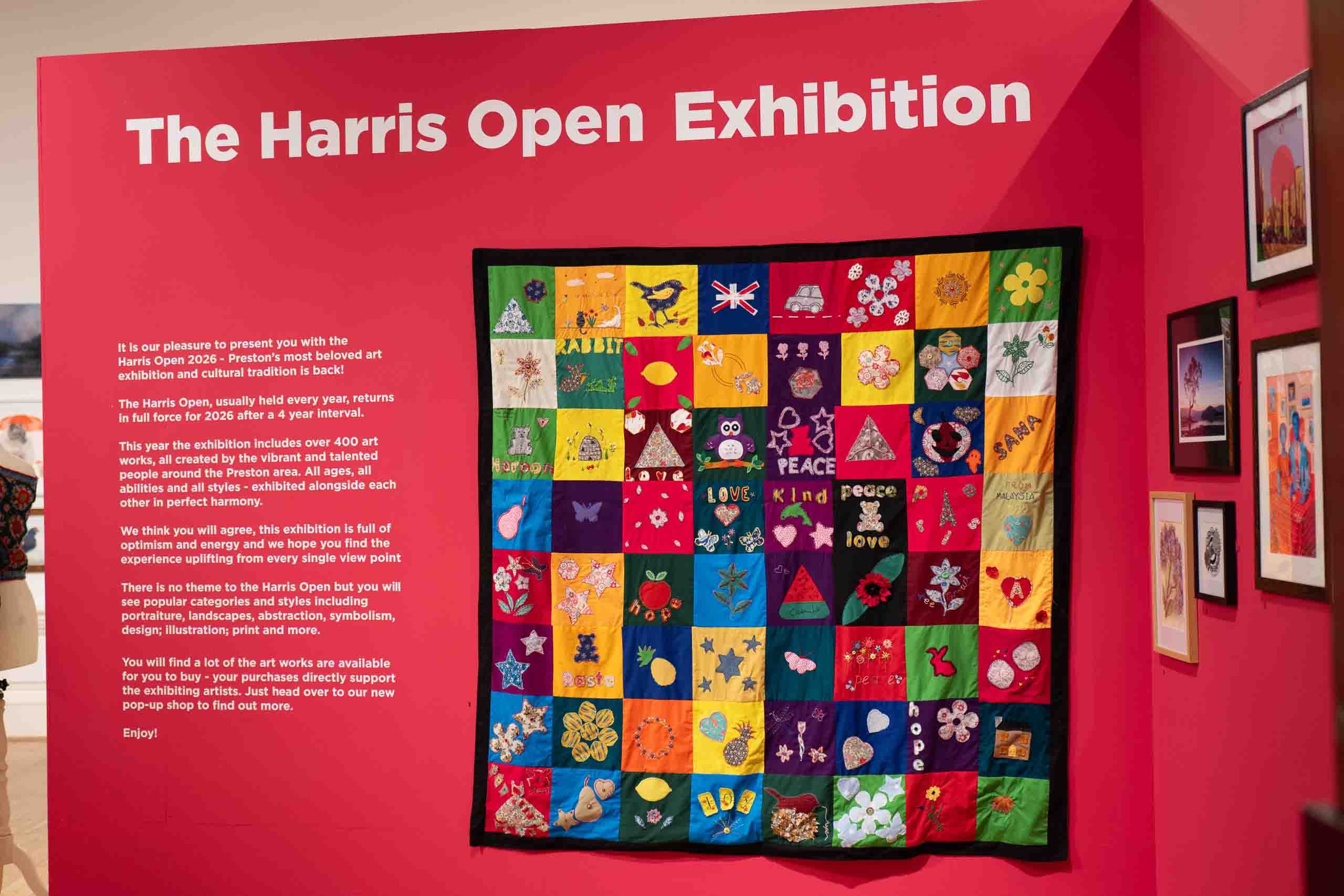 Harris Museum Open Exhibition 2026 Preston — exhibition entrance sign panel beside a large colourful quilted textile artwork on the red feature wall